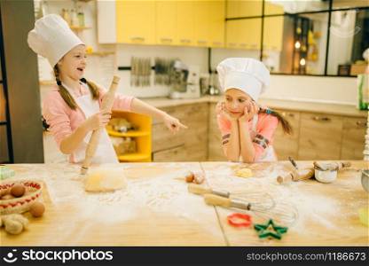 Two little girls chefs are laughing, cookies preparation on the kitchen. Kids cooking pastry and having fun, children cooks preparing cake, happy childhood