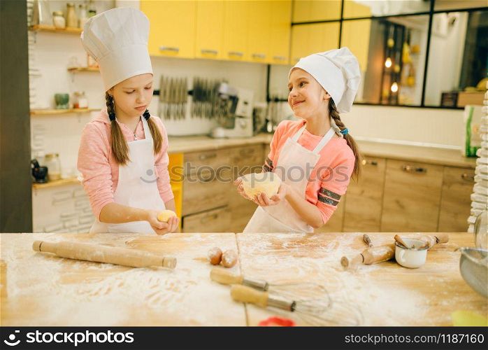 Two little girls chefs roll out the dough with rolling pins, cookies preparation on the kitchen. Kids cooking pastry and having fun, children cooks preparing cake. Little chefs roll out the dough with rolling pins