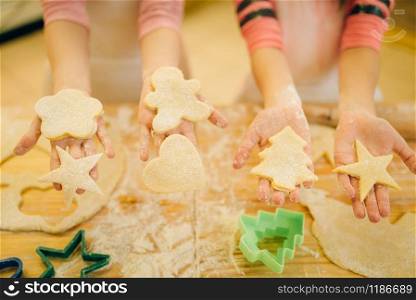 Two little girls chefs show the dough cut out by cookie cutters, bakery preparation on the kitchen, funny bakers. Kids cooking pastry and having fun, children cooks preparing cake. Little chefs show dough cut out by cookie cutters