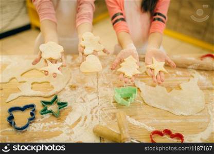 Two little girls chefs show the dough cut out by cookie cutters, bakery preparation on the kitchen, funny bakers. Kids cooking pastry and having fun, children cooks preparing cake