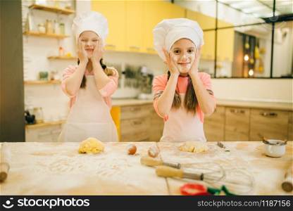 Two little girls chefs smears their faces with flour, cookies preparation on the kitchen. Kids cooking pastry and having fun, children preparing cake