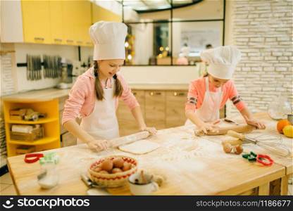 Two little girls chefs with rolling pins, cookies preparation on the kitchen, funny bakers. Kids cooking pastry and having fun, children cooks makes dough and preparing cake. Little girls chefs with rolling pins, funny bakers