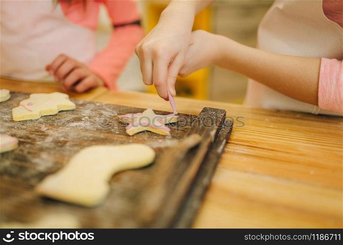 Two little girls cooks cover the cookies with a sweet layer, bakery preparation on the kitchen, funny bakers. Kids cooking pastry, children chefs preparing cake