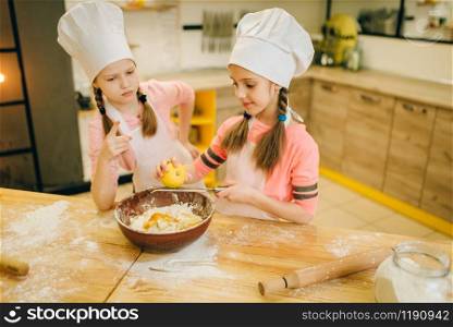 Two little girls cooks in caps rubs lemon to the bowl, cookies preparation on the kitchen. Kids cooking pastry, children chefs preparing cake