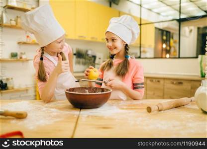 Two little girls cooks in caps sniffing sweet vanilla powder, cookies preparation on the kitchen. Kids cooking pastry, children chefs preparing cake. Little girls cooks in caps sniffing vanilla powder