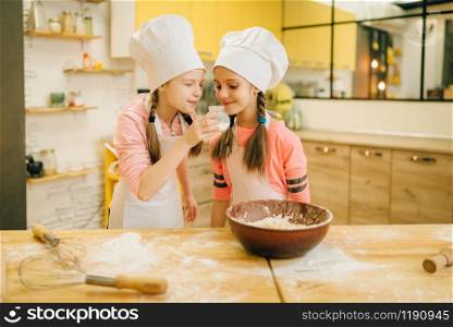 Two little girls cooks in caps sniffing sweet vanilla powder, cookies preparation on the kitchen. Kids cooking pastry, children chefs preparing cake