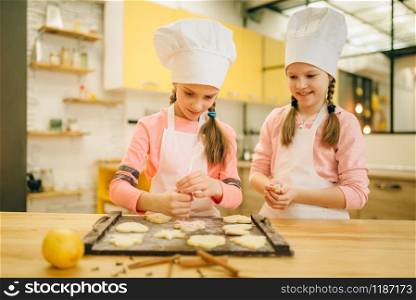 Two little girls cooks preparing to send cookies in the oven, bakery preparation on the kitchen, funny bakers. Kids cooking pastry and having fun, children chefs prepares cake