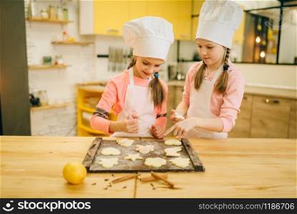 Two little girls cooks spread out cookies on a wooden board, bakery preparation on the kitchen, funny bakers. Kids cooking pastry, children chefs preparing cake. Two little girls cooks spread out cookies on board