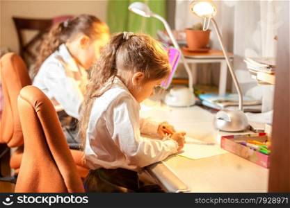 Two little girls drawing pictures behind desk