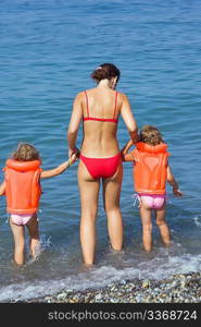 two little girls in lifejackets with young woman coming into sea