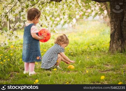 Two little girls in the park under the blossom tree, play with balls