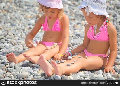 two little girls is playing with pebble stones. focus on girl with white panama hat on her head.