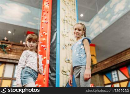 Two little girls looks on climbing wall, children game center. Excited childs having fun on playground indoors. Kids playing in amusement centre. Little girls looks on climbing wall, game center