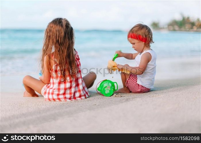 Two little girls making sand castle on the white tropical beach. Two kids making sand castle and having fun at tropical beach