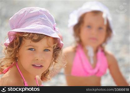 two little girls on a sea coast. focus on girl wearing pink panama hat. another girl in out of focus.