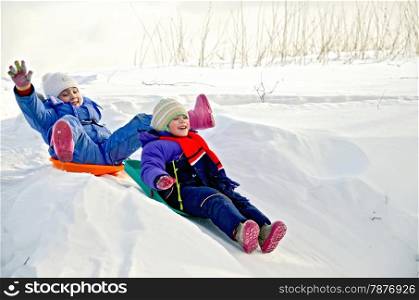 Two little girls on a sled sliding down a hill on snow in winter