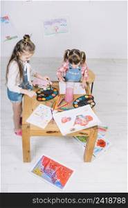 two little girls painting with aquarelle paper table