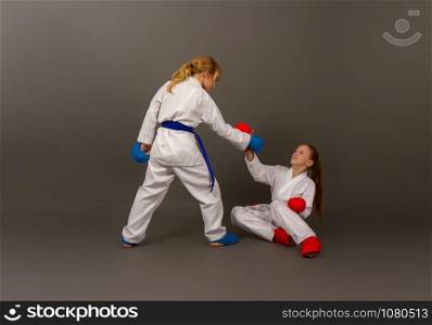 two little karate girls in a kimono and full sports protective gear of red and blue colors help an opponent who has fallen in battle to climb.. karate girls figters