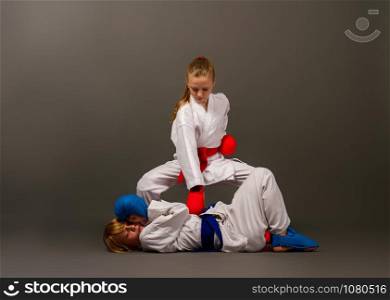two little karate girls in kimonos and full sports protective gear of red and blue fight against a dark background. karate girls figters