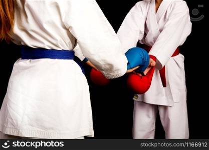 Two little karate women in white kimonos, one in red and the other in blue competition equipment shake hands as a sign of respect before the fight against a dark background. karate girls greeting
