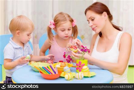Two little kids with young teacher paint Easter eggs, art lesson, interacting children in daycare, Christian holiday concept&#xA;