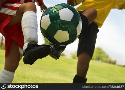 Two little league players (7-9 years) kicking ball mid air, mid section, close up