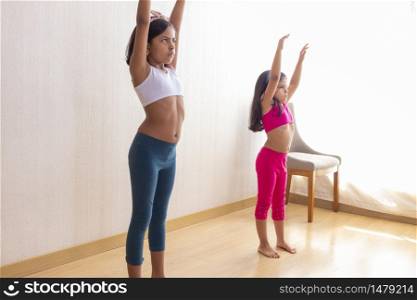Two little sisters are doing exercise routines in the living room at home