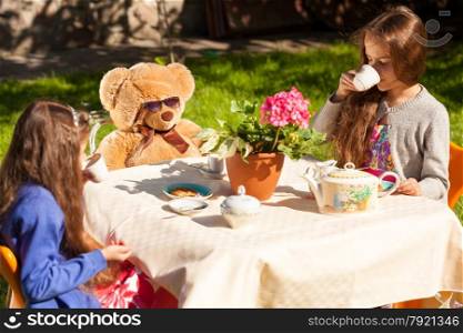 Two little sisters having english breakfast with teddy bear at yard