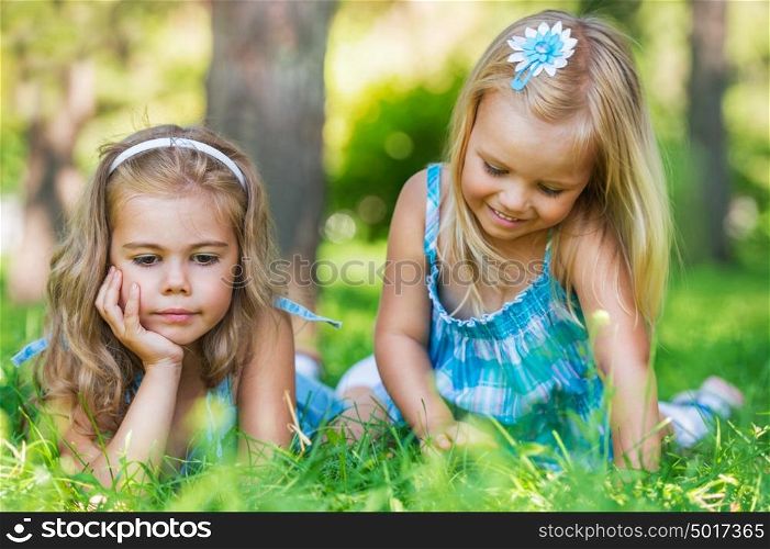 Two little sisters having fun in summer park while laying on lawn