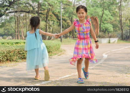 Two little sisters holding each other hands in a summer green park.