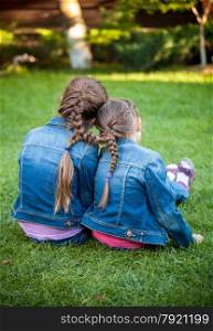 Two little sisters sitting on grass head to head with joint braids