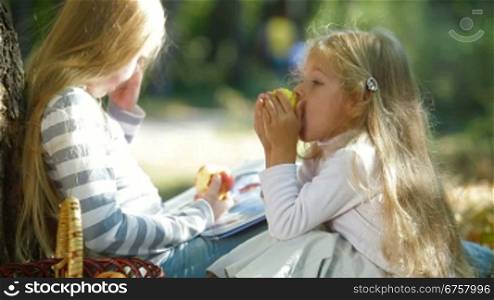 Two little sisters spending time together in the park, reading a book