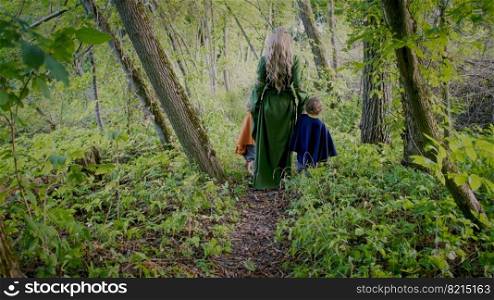Two little toddler boys cosplay gnomes or hobbits with elf woman walking in green forest. Unrecognizable fairy tale characters. Halloween, kids concept. Amazing light. High quality photo. Two little toddler boys cosplay gnomes or hobbits with elf woman walking in green forest. Unrecognizable fairy tale characters. Halloween, kids concept. Amazing light.