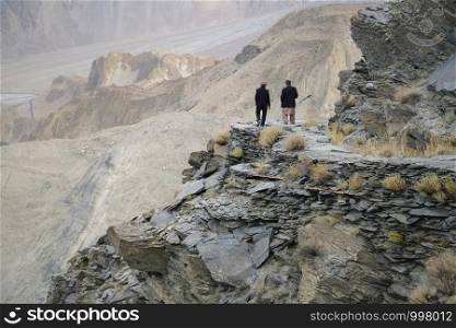 Two local Pakistani men talking and walking along the way to Passu glacier surrounded by wilderness mountain range, Passu, Gilgit Baltistan, Pakistan.