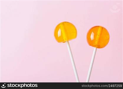 Two lollipops on white plastic sticks on pink pastel background with copy space