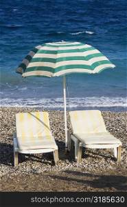 Two lounge chairs under a beach umbrella on the beach, Greece