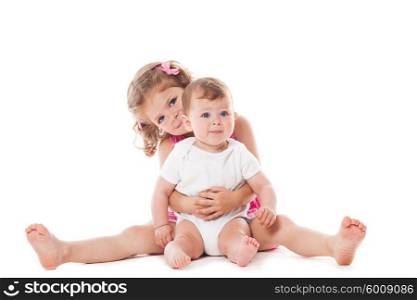 Two lovely sisters sitting on the floor and smiling isolated on white. Two sisters isolated
