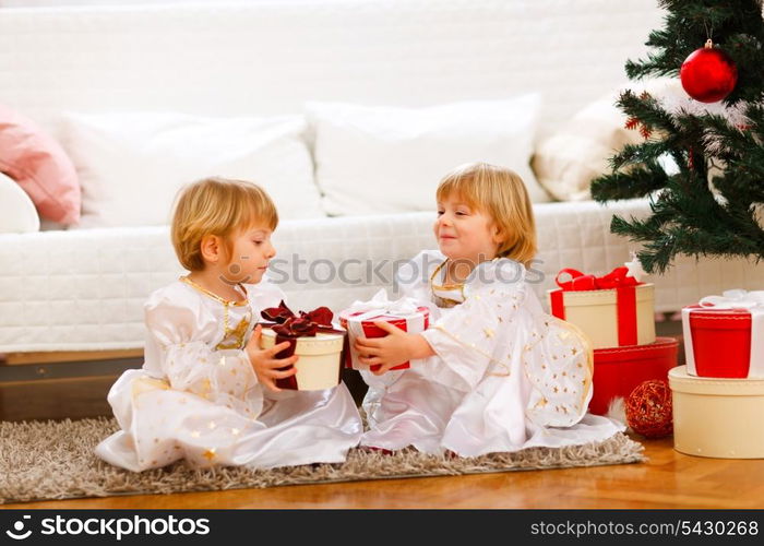 Two lovely twins girl exchanging presents near under Christmas tree