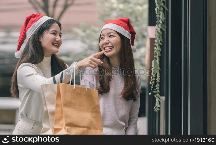 Two lovely women holding bags while doing window shopping at department store in Christmas season. New Year Celebration and Sales Discount Concept.