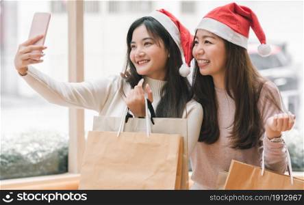 Two lovely women taking photo, selfie and holding shopping bags at department store in Christmas season. New Year Celebration and Sales Discount Concept.