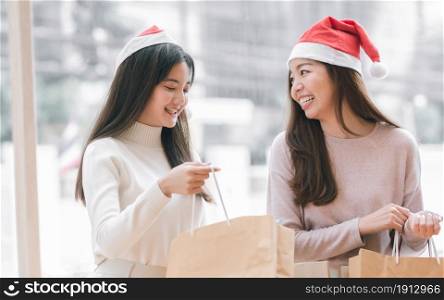 Two lovely women wearing santa hat and holding paper shopping bags for christmas or new year celebration. Sales Discount Concept.