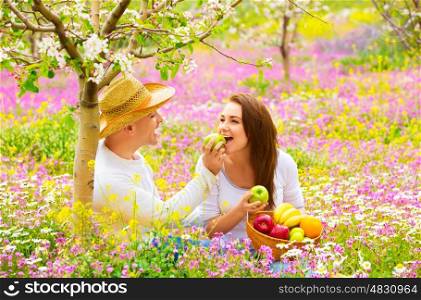 Two lovers on picnic in beautiful spring garden, purple flowers field, blooming tree, handsome man feeding girlfriend green apple
