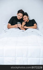 Two loving women sleeping and playing smartphones.