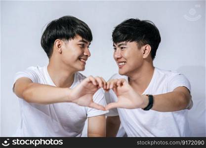 Two loving young men look at each other and make a hand of love symbol.
