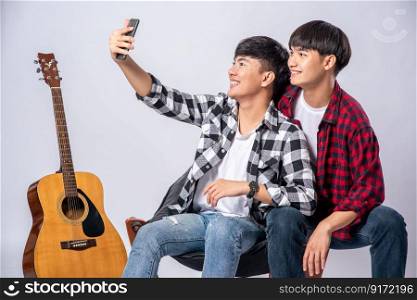 Two loving young men sit on a chair and take a selfie from a smartphone.