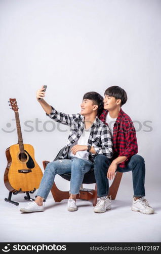 Two loving young men sit on a chair and take a selfie from a smartphone.