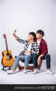 Two loving young men sit on a chair and take a selfie from a smartphone.