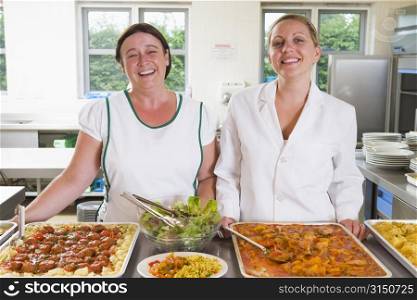 Two lunch ladies standing behind full lunch service station