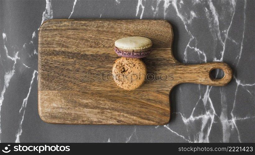 two macaroons wooden chopping board marble backdrop