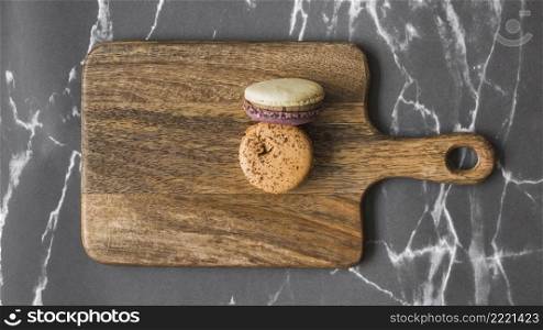two macaroons wooden chopping board marble backdrop